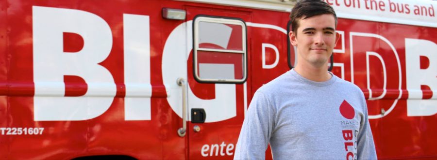 Andrew Schuler stands in front of OneBlood’s Big Red Bus. Photo by Cat Keve.